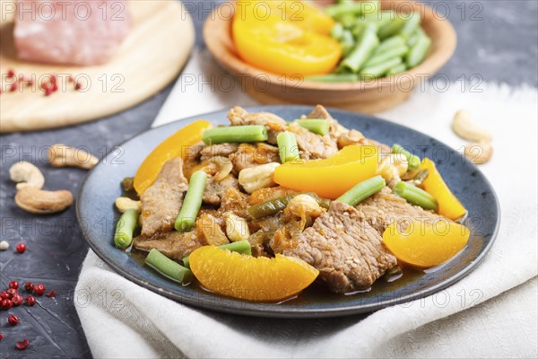 Fried pork with peaches, cashew and green beans on a black concrete background. Side view, close