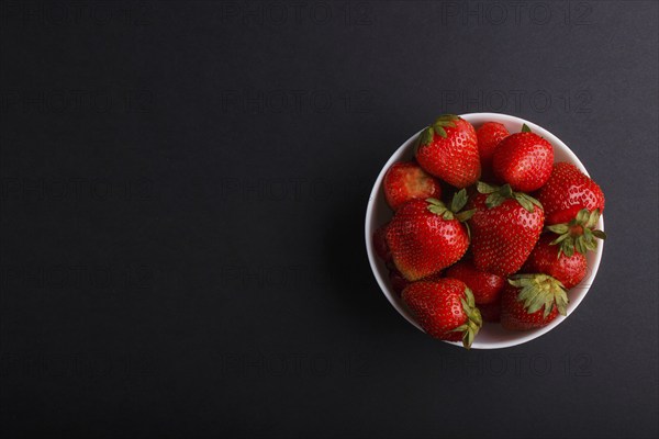 Fresh red strawberry in white bowl on black background. top view, flat lay, copy space