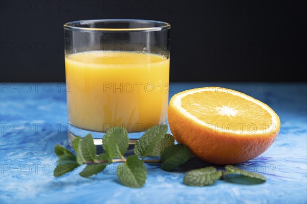 Glass of orange juice with mint on a black and blue background. Hard light, contrast. Side view,