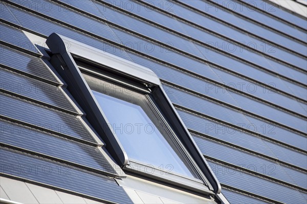 Roof window on a detached house with solar roof tiles. Solar tiles are a beautiful and high-quality