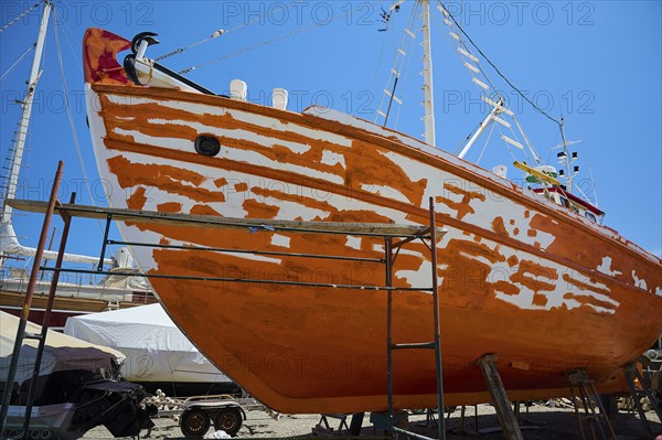 A wooden boat is being restored in dry dock, with the orange and white colour being renewed, Patmos