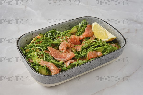 A vibrant salad features fresh smoked salmon slices mixed with crisp arugula and cucumber,