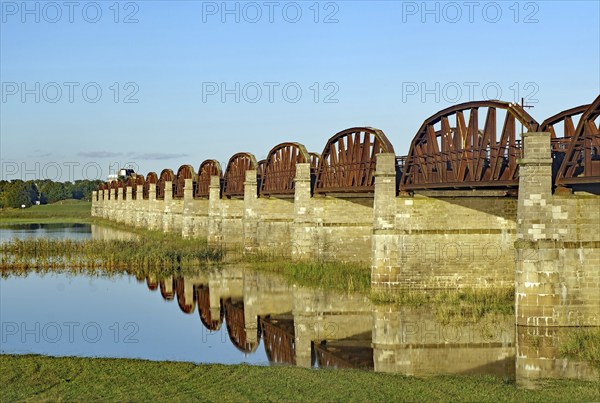 Close-up of stone bridge pillars and the calm water below reflecting the bridge on a clear day,