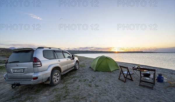 Camping on the lakeshore, off-road vehicle next to tent and camping chairs, sunset at Issyk Kul
