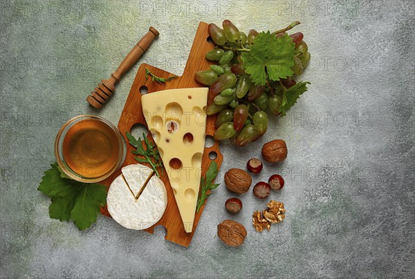 Cheese with big holes, emmental, maasdam, brie cheese, on a cutting board, with grapes and honey,