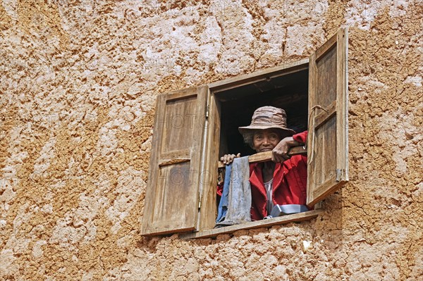 Elderly Malagasy woman looking from window in two stories mud house in the Ambositra District,