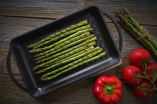 Asparagus grilled on cast iron grill pan on wood table with tomatoes and pepper