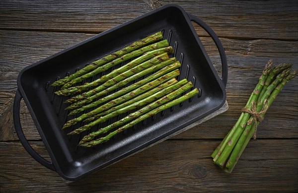 Asparagus grilled on cast iron grill pan on wood table with tomatoes and pepper