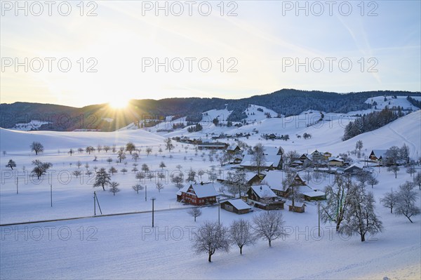 Snow-covered village in winter landscape at sunrise, surrounded by rolling hills, Menzingen, Zug,