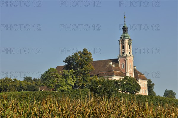 Baroque church stands majestically in the midst of a green landscape under a clear blue sky,