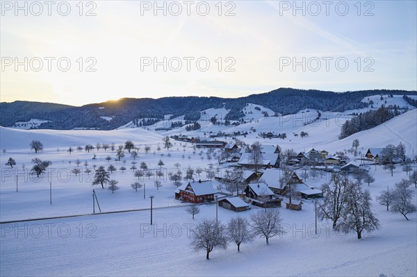 Snow-covered village in winter landscape at sunrise, surrounded by rolling hills, Menzingen, Zug,