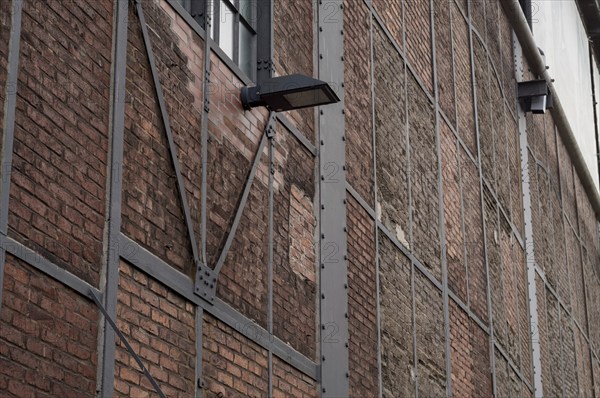 Weathered brick wall with metal supports and lamps, highlighting the industrial history of a