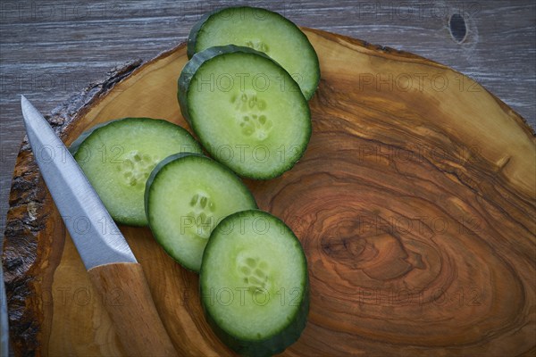 Cucumber slices in and olive wood board with knife