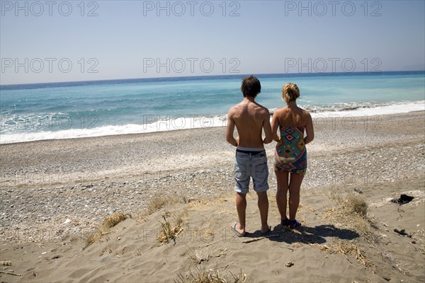 Model released brother and sister twins stand on sandy beach looking out to sea, Rhodes, Greece,