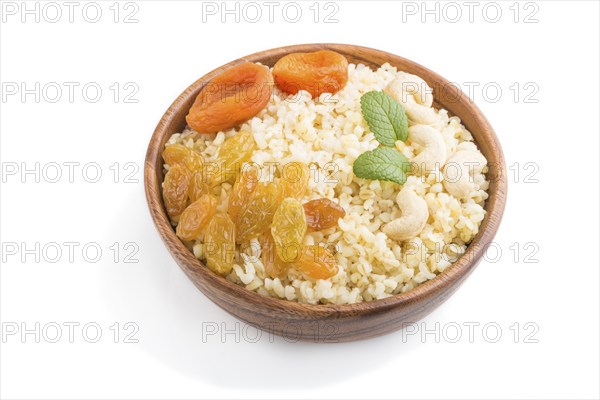 Bulgur porridge with dried apricots, raisins and cashew in wooden bowl isolated on white background