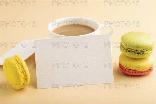 White paper business card mockup with yellow and green macaroons and cup of coffee on orange pastel