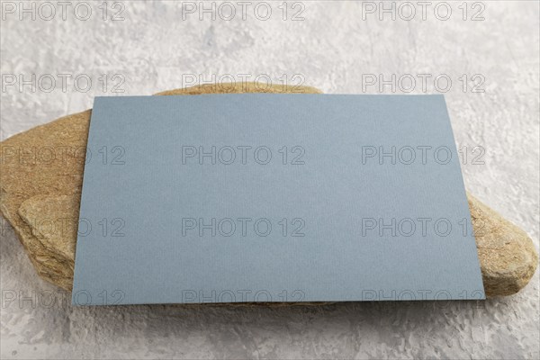 Blue paper business card, mockup with natural stone on gray concrete background. Blank, side view,
