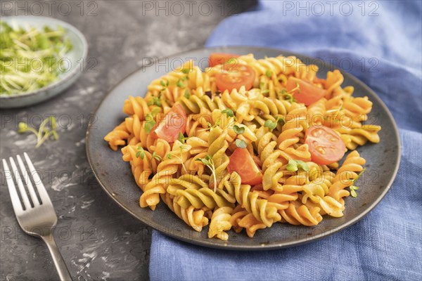 Tortiglioni semolina pasta with tomato and microgreen sprouts on a black concrete background and