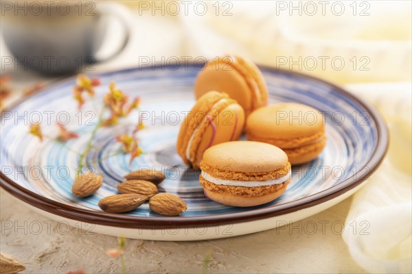 Orange macarons or macaroons cakes with cup of coffee on a white concrete background and linen