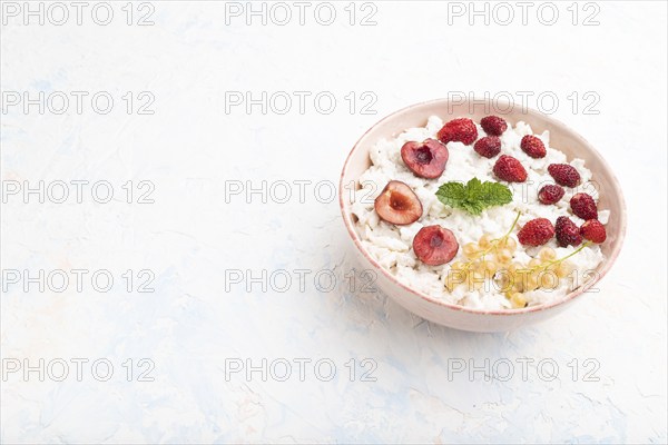 Rice flakes porridge with milk and strawberry in ceramic bowl on white concrete background. Side