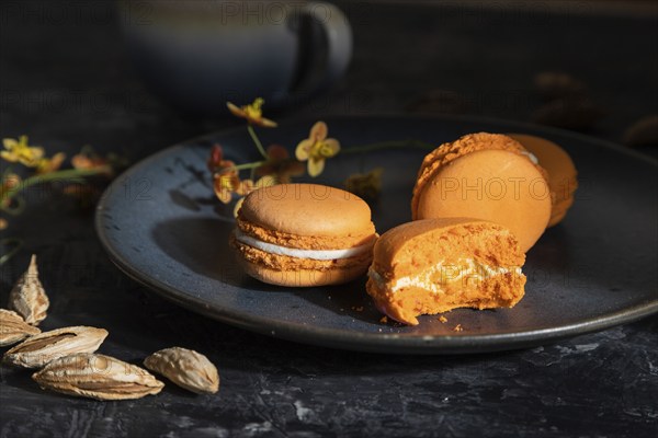 Orange macarons or macaroons cakes with cup of coffee on a black concrete background. Hard light,