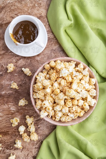 Popcorn with caramel in ceramic bowl on brown concrete background and green textile. Top view, flat