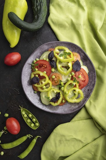Vegetarian salad from green pea, tomatoes, pepper and basil on a black concrete background and