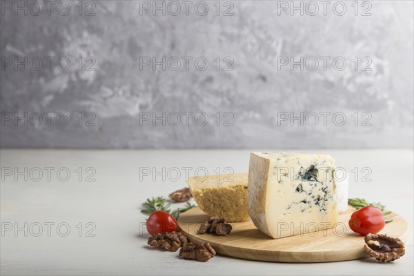 Blue cheese and various types of cheese with rosemary and tomatoes on wooden board on a white and