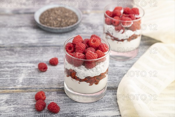 Yogurt with raspberry, goji berries and chia seeds in glass on gray wooden background and linen