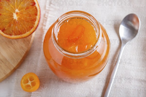 Orange and kumquat jam in a glass jar with fresh fruits on a white linen tablecloth. Homemade,