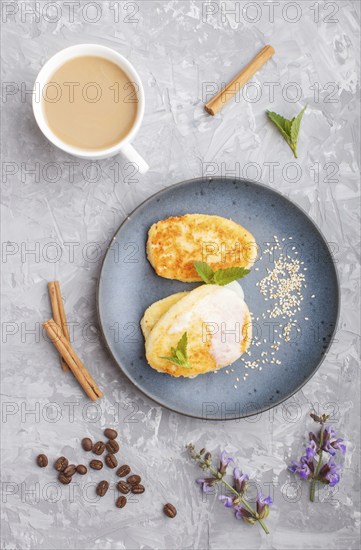 Cheese pancakes on a blue ceramic plate and a cup of coffee on a gray concrete background. top