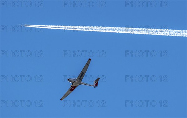 Twin-engine jet, passenger aircraft, with contrails, in the sky, below a motorised sailplane