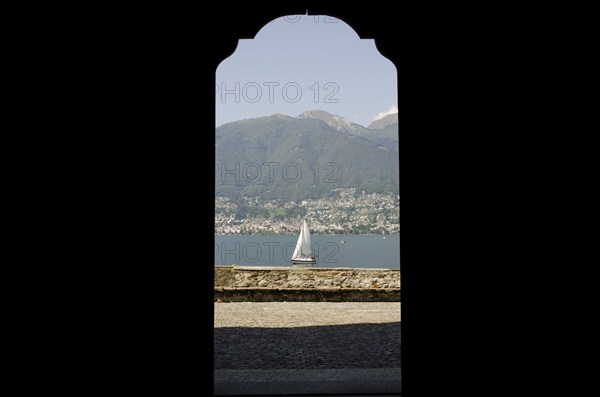 Looking at a Sailing Boat Through an Open Door on Lake Maggiore with Mountain in a Sunny Summer Day