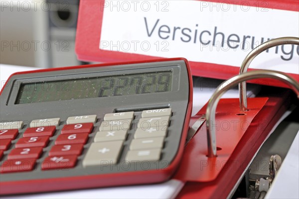 Symbolic image: Folder with insurance policies and calculator on a desk