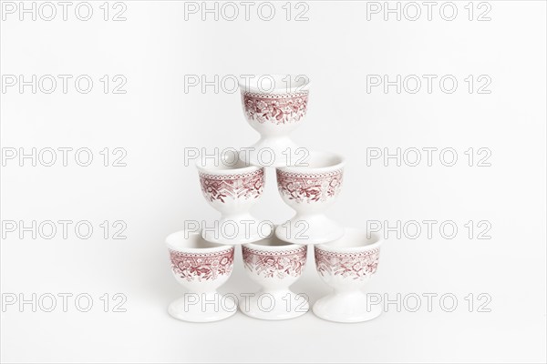 Symmetrically stacked ceramic egg cups with a reddish pattern on a white background