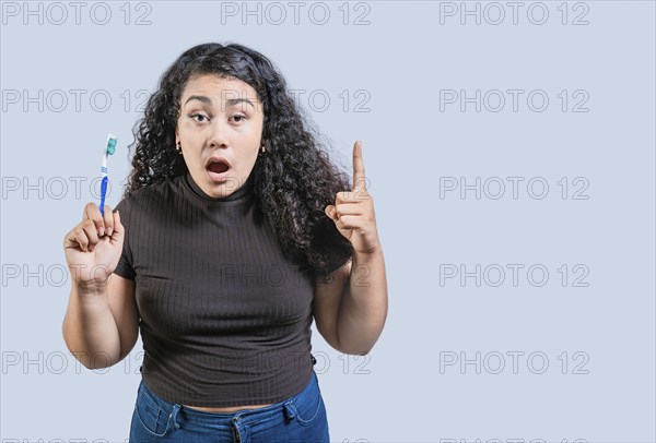 Surprised woman holding toothbrush pointing up. Amazed girl holding toothbrush and pointing up
