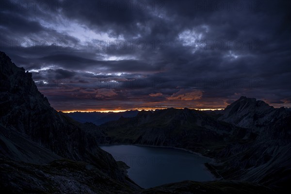 Lake Lüner See with Montafon mountains and dramatic cloudy sky at sunrise, Tschagguns, Rätikon,
