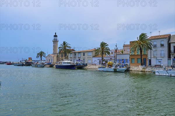 Coastal town with colourful houses and palm trees, boats in the water and a lighthouse, on a sunny