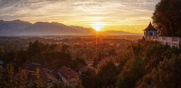 A picturesque sunset over an autumnal landscape with mountains and a building in the foreground,