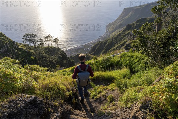 Young man looking out to sea on cliff, evening mood, green coastal landscape on cliff, sea and