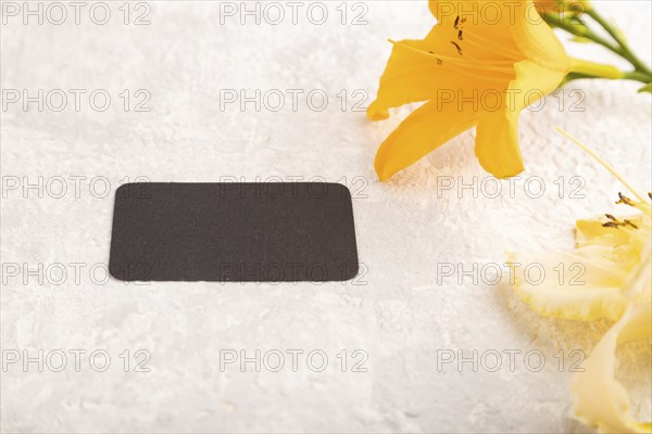 Black paper business card mockup with orange day-lily flower on gray concrete background. Blank,