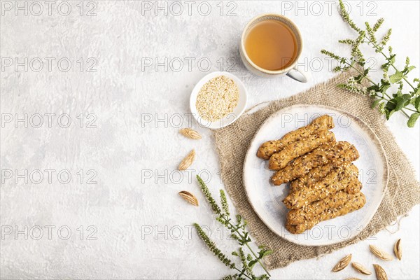 Crumble cookies with seasme and almonds on ceramic plate with cup of green tea and linen textile on