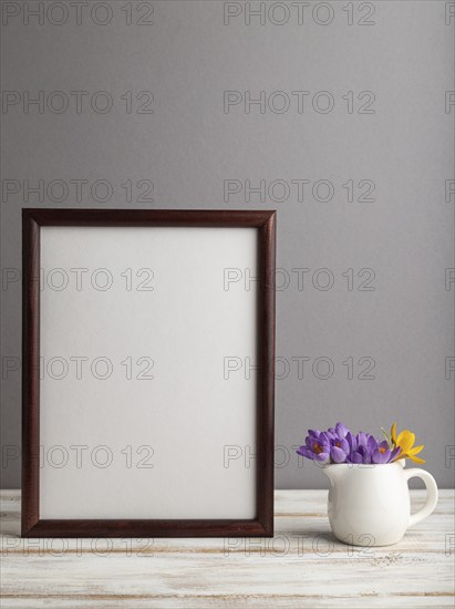 Brown wooden frame mockup with snowdrop crocus flowers on gray paper background. Blank, vertical