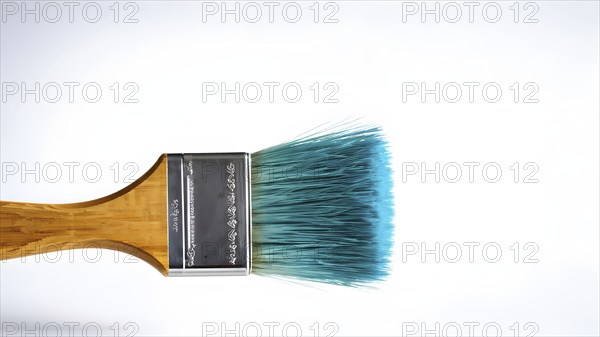 Thick paintbrush dipped in cyan bristles dripping onto a white background, AI generated