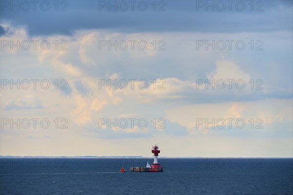 A red lighthouse stands on a calm, blue sea under a slightly cloudy sky, with a pilot boat,