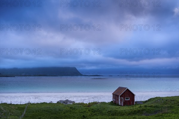 A red wooden hut on the sandy beach of Ramberg (Rambergstranda), sea and mountains. At night at the
