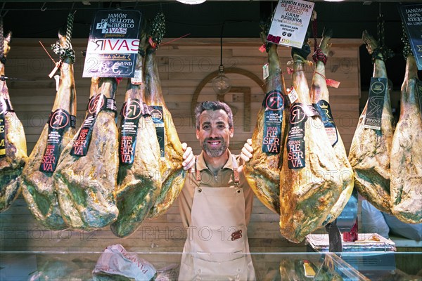 Castilian man, 40 years old, between Iberico hams for sale at the Mercado Central, Salamanca,