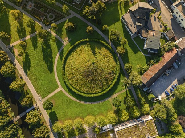 Aerial view of a green Celtic burial mound with circular path surrounded by houses and trees,