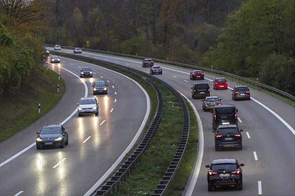 Motorway with several cars at dusk, headlights switched on, surrounded by trees, Rems-Murr