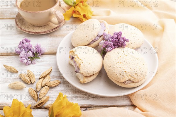 Meringues cakes with cup of coffee on a white wooden background and orange linen textile. Side